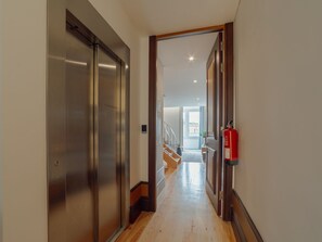 Ein Flur mit einem metallenen Aufzug und einer Holztür, die zu einer Treppe führt.