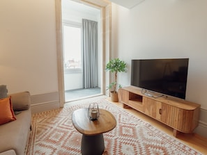 Ein modernes Wohnzimmer mit Flachbildfernseher, einer Holz-Unterhaltungseinheit, einer Couch, einem Couchtisch und einem gemusterten Teppich.