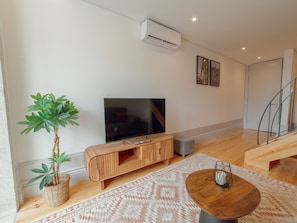 A modern living room with a flat-screen TV, wooden entertainment unit, a round coffee table, a patterned rug, and a staircase. - Apartment  by Interhome (Porto)