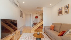 A modern living room with a flat-screen TV, wooden furniture, a patterned rug, and a staircase leading to another level. - Apartment  by Interhome (Porto)