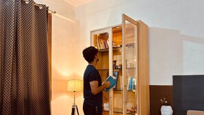 Een persoon staat in een kamer met een glazen kast vol boeken en decoratieve objecten.