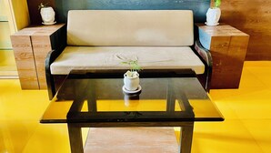 Een moderne zithoek met een bank, een tafel met glazen blad en twee bijzettafels met decoratieve vazen.
