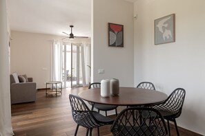 Un comedor con una mesa redonda, sillas negras y dos jarrones. Se observa un sofá y una pequeña mesa al fondo.