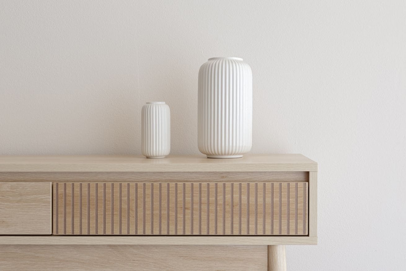 A wooden cabinet with two white vases on top.