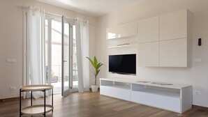 Ein modernes Wohnzimmer mit Flachbildfernseher, weißen Schränken und einem runden Holztisch.