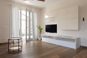 A modern living room with a flat-screen TV, white cabinetry, and a round wooden table. - Domio - Elegant Oasis with Terrace (Pisa)