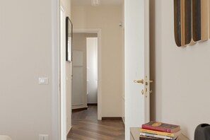 A hallway with a wooden floor, a white door with a brass handle, and a stack of books on a small table. - Domio - Elegant Oasis with Terrace (Pisa)