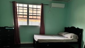 Una habitación con una cama, un aparador, una ventana con cortinas y un equipo de aire acondicionado.