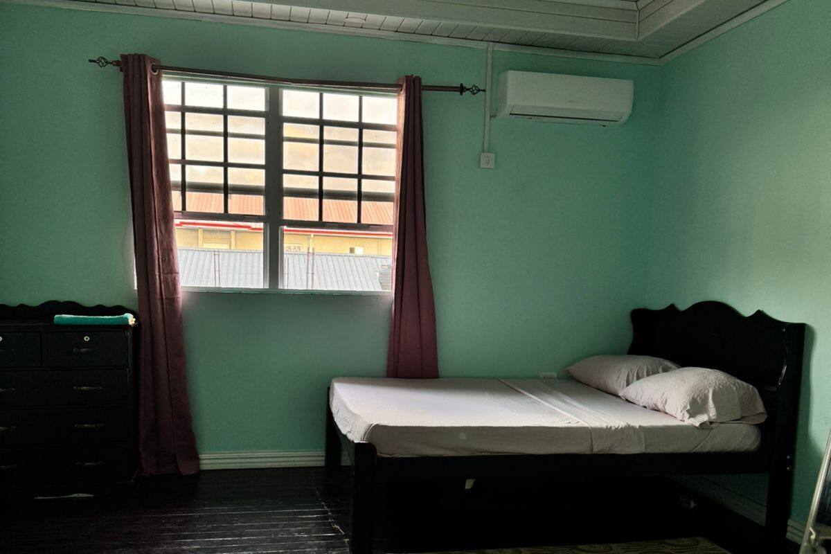 Una habitación con una cama, un aparador, una ventana con cortinas y un equipo de aire acondicionado.
