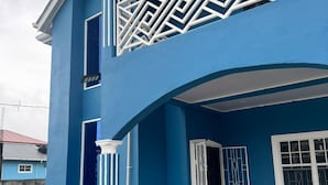 Un edificio de dos pisos con fachada azul, detalles blancos y un balcón con barandilla geométrica.