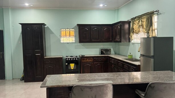 Una cocina con armarios de madera oscura, encimera de granito, estufa a gas, microondas y refrigerador.
