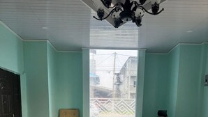 Una habitación con paredes verde azulado, un ventanal grande, una puerta de madera, un escritorio blanco y una silla de oficina negra.