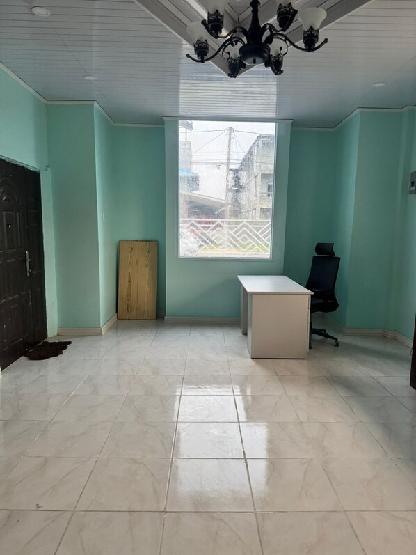 A room with teal walls, a large window, a wooden door, a white desk, and a black office chair.