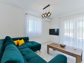 Ein Wohnzimmer mit einem türkisfarbenen Sofa, einem Holztisch, einem Flachbildfernseher und einer Deckenleuchte.