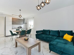 Un saló modern amb un sofà color turquesa, una taula de centre de fusta i una zona de menjador amb cadires, amb una cuina al fons.