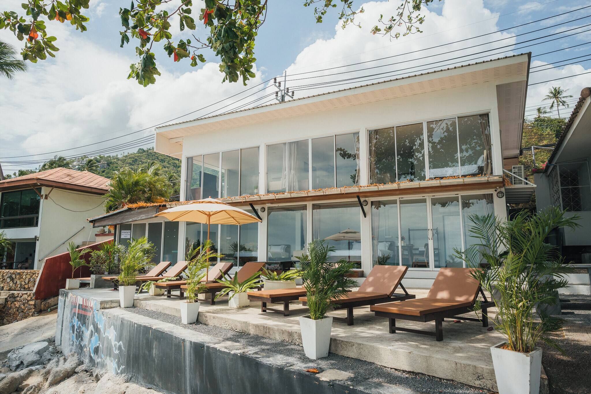 A modern building with large windows, a pool area with lounge chairs, and potted plants.
