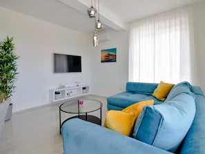 Un salon moderne avec un canapé bleu, une table basse en verre, un téléviseur à écran plat et une plante en pot.