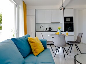 Un salon moderne comprenant un canapé, une table à manger avec des chaises et un coin cuisine avec des placards et des appareils électroménagers.