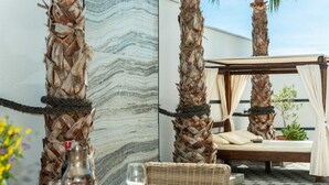 An outdoor dining area with a table set for two, surrounded by woven palm fronds, a wicker chair, and a bench with a cushion. - Vacation home  by Interhome (Rovanjska)