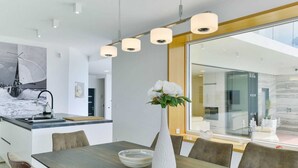 A modern kitchen with a large island, pendant lighting, and a dining area with a vase of flowers. - Vacation home  by Interhome (Rovanjska)