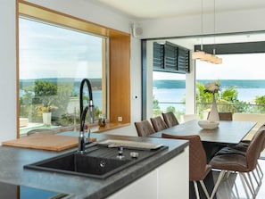 A modern kitchen with a large island, a dining area with a view of the sea, and a large window. - Luxury Villa Michele with infinity pool by Interhome (Rovanjska)