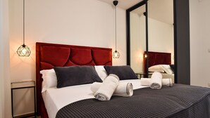 Ein ordentlich bezogenes Bett mit Kissen und Handtüchern, ein rotes, mit Stoff überzogenes Kopfteil und ein großer Spiegel an der Wand.