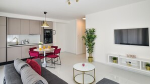 Ein modernes Wohnzimmer mit einem grauen Sofa, roten Sesseln, einem kleinen weißen Tisch und einem an der Wand befestigten Fernseher.