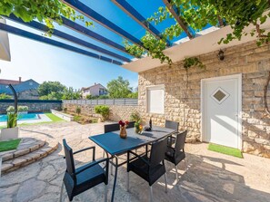 An outdoor patio with a table and chairs, a stone wall, and a pool in the background. - Vacation home  by Interhome (Pridraga)
