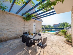 A patio with a table and chairs, a stone wall, and a pool in the background. - Dalmatian Holiday house Marcella with pool by Interhome (Pridraga)