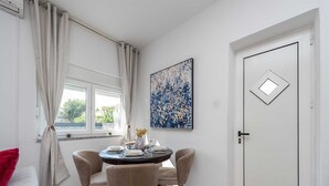 Een eetruimte met een ronde tafel, vier stoelen, een vaas met bloemen en een schilderij aan de muur.