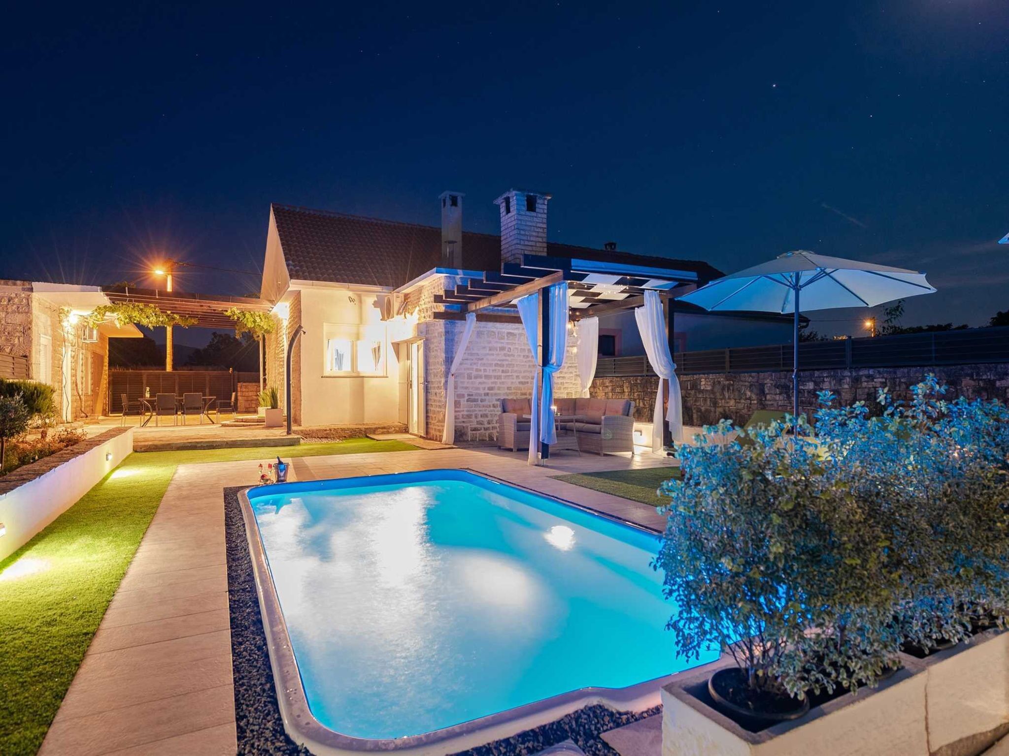 A swimming pool with a pergola and outdoor seating area at dusk.