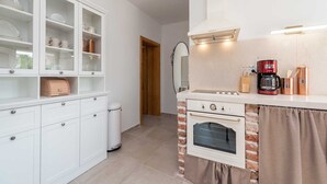 Een kleine keuken met witte kasten, een inbouwoven, een koffiezetapparaat en een accentmuur van baksteen.