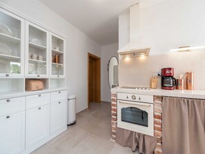 A compact kitchen with white cabinetry, a built-in oven, a coffee maker, and a brick accent wall. - Vacation home  by Interhome (Pridraga)