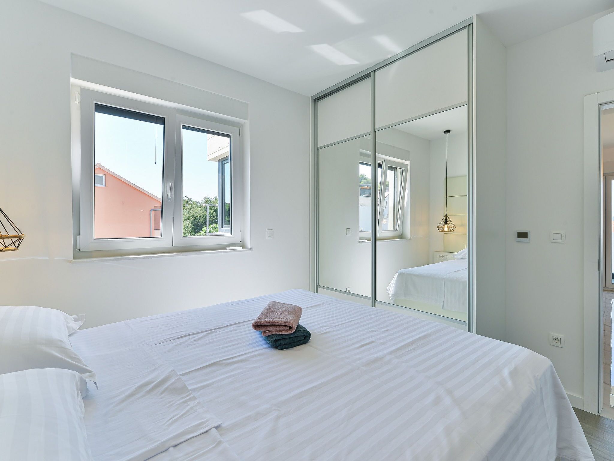 A bedroom with a bed, a window, a mirror, and a door.