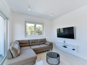 A modern living room with a sectional sofa, a flat-screen TV mounted on the wall, and a round coffee table. - Apartment  by Interhome (Zadar/Bibinje)