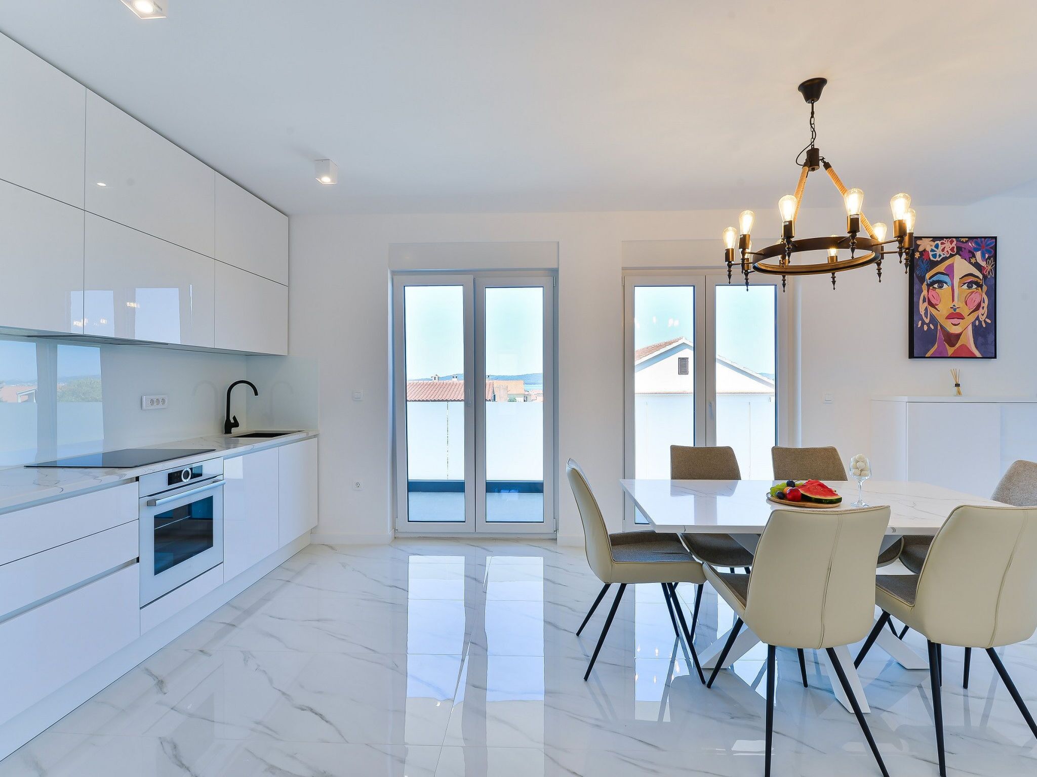 Uma cozinha moderna com armários brancos, forno embutido e um espaço de jantar com mesa e cadeiras.