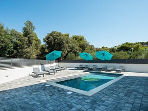 Uma piscina com espreguiçadeiras e guarda-sóis, rodeada por árvores e um céu claro.