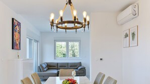 Ein Essbereich mit einem Marmortisch, vier Stühlen, einer Chandelierleuchtre und einem Sofa im Hintergrund.
