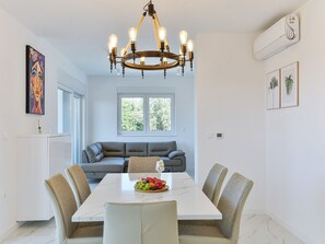 A dining area with a marble table, four chairs, a chandelier, and a sofa in the background. - Apartment  by Interhome (Zadar/Bibinje)