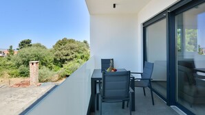 Ein Balkon mit Tisch und Stühlen, eine kleine Ziegelstruktur und Blick auf Bäume und Gebäude.