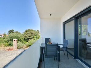 A balcony with a table and chairs, a small brick structure, and a view of trees and buildings. - Apartment  by Interhome (Zadar/Bibinje)