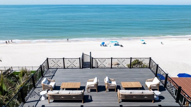 Blick auf den Strand von einer Terrasse mit Liegestühlen und Sonnenschirmen.