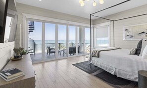 A bedroom with a large bed, a desk with a book, a chair, and a balcony with a view of the sea. - Sea Swept | Luxury Beachfront Estate (Bradenton Beach)