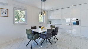 Una cocina moderna con armarios blancos, encimera de mármol y comedor con mesa y sillas blancas.