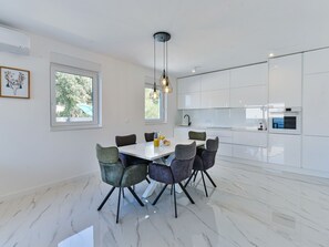 Eine moderne Küche mit weißen Schränken, einer Marmorarbeitsplatte und einem Essbereich mit weißem Tisch und Stühlen.