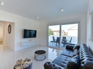 A modern living room with a flat-screen TV, a sofa, a round ottoman, and a dining area visible through large sliding glass doors. - Villa Div with heated pool Apartment No.1 by Interhome (Zadar/Bibinje)