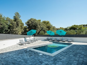 A swimming pool with lounge chairs and umbrellas, surrounded by trees and a clear sky. - Villa Div with heated pool Apartment No.1 by Interhome (Zadar/Bibinje)