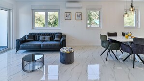 Una sala moderna con un sofá de cuero negro, una mesa de comedor con sillas y un piso de mármol.