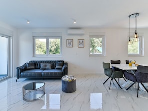 Ein modernes Wohnzimmer mit einer schwarzen Ledersofa, einem Esstisch mit Stühlen und einem Marmorboden.