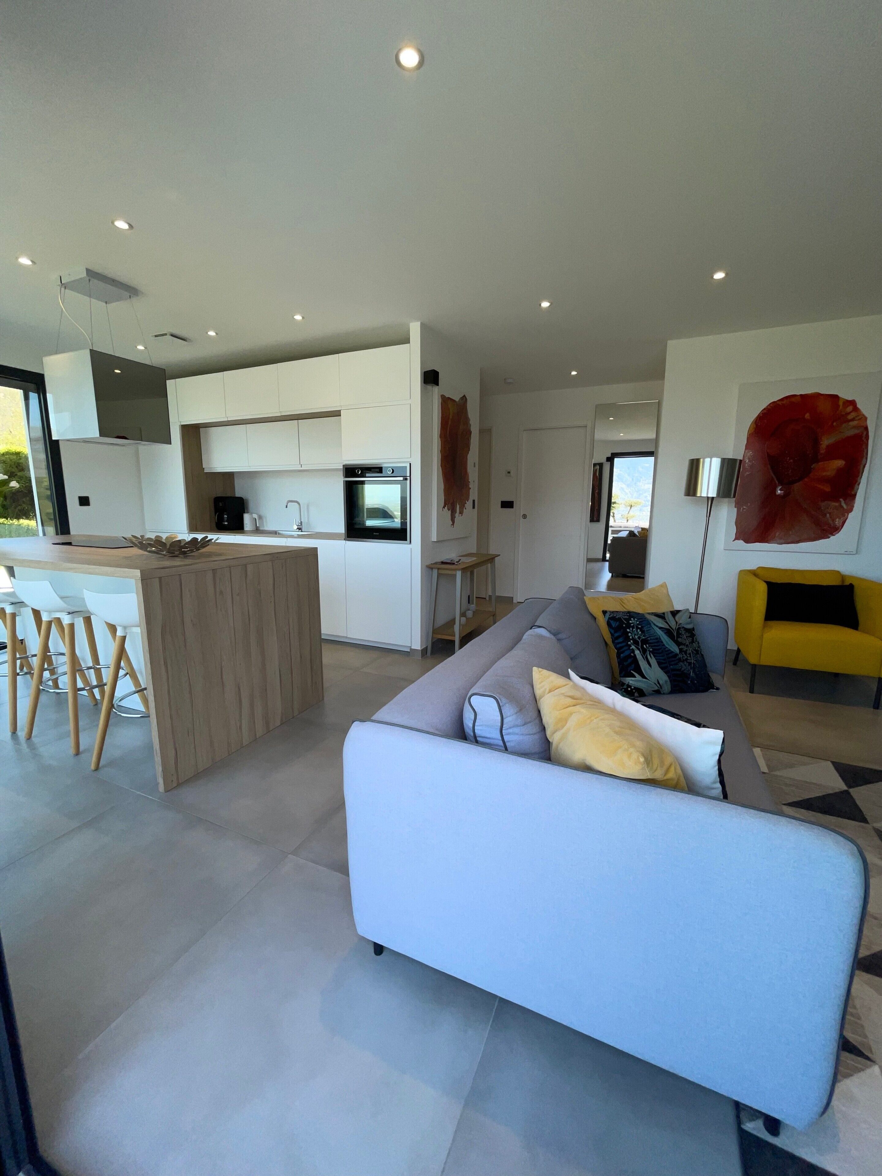 Une cuisine moderne avec des meubles blancs, un four encastré et un coin repas comprenant une table et des chaises blanches.